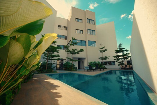 Piscina do CLATT Hotel com paisagismo, deck, cadeiras de sol, mesa com guarda-sol.
