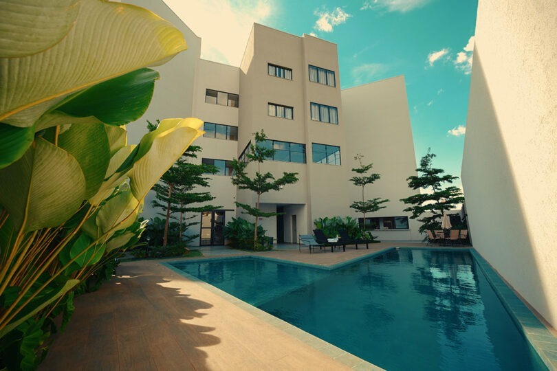 Piscina do CLATT Hotel com paisagismo, deck, cadeiras de sol, mesa com guarda-sol.