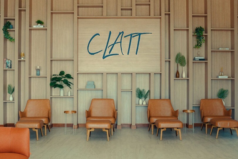 Lobby do CLATT Hotel com painel de design contemporâneo feito em madeira e logo do Clatt embutido, além de livros e vasos decorativos e poltronas com encosto para os pés e mesinhas de apoio
