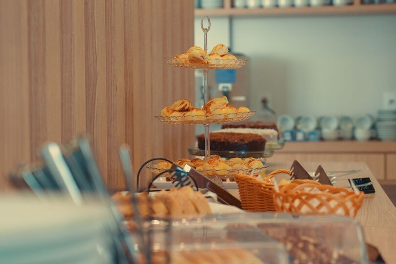 Buffet de café da manhã do CLATT Hotel com pães, bolos, comidas quentes e bebidas variadas.